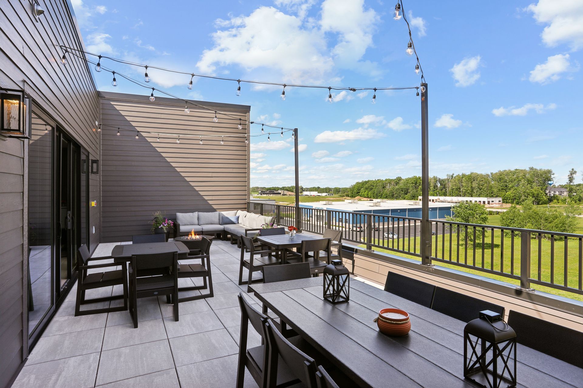 Outdoor deck with tables, chairs, string lights, and a river view under a blue sky