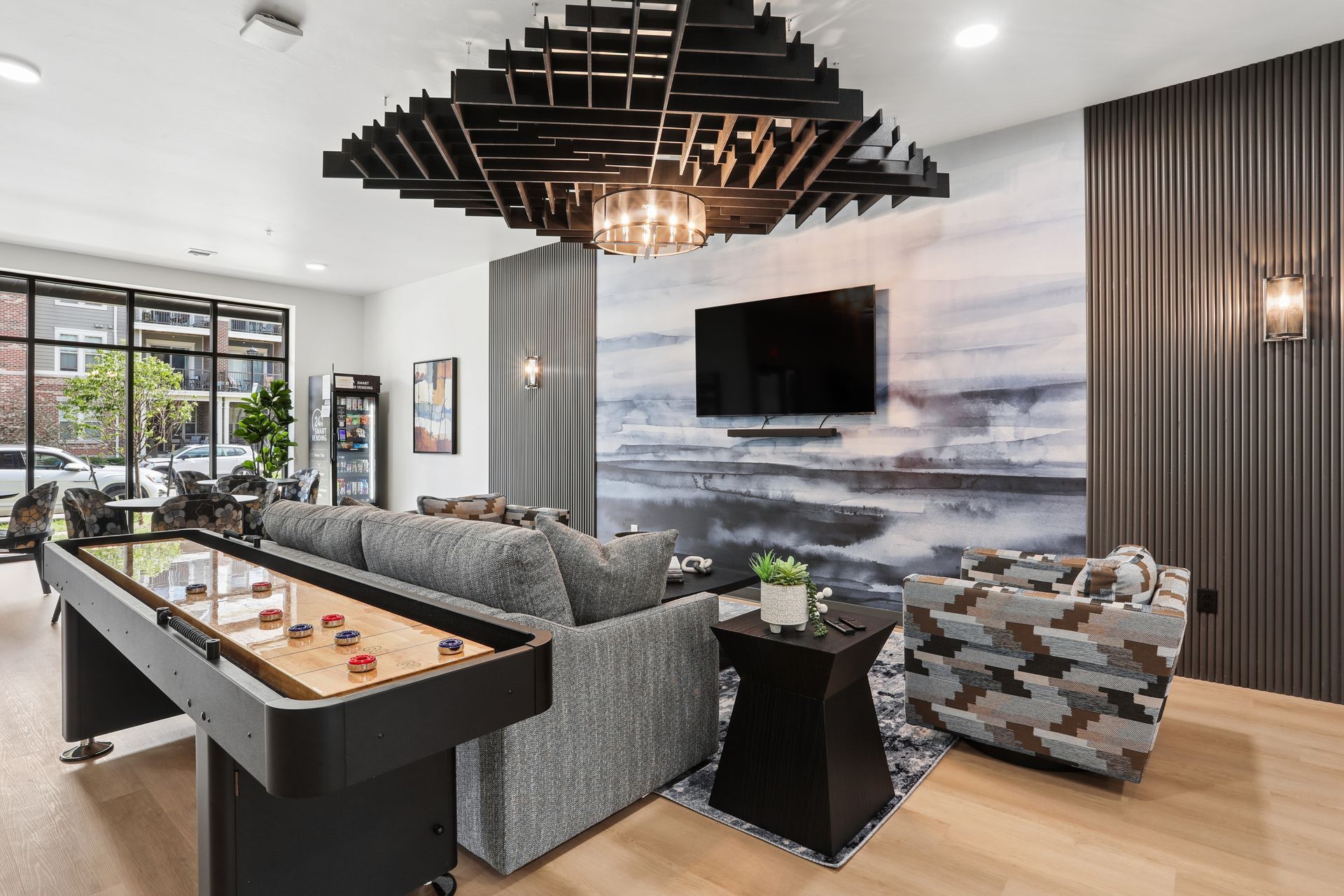 Modern lounge with gray sectional, pool table, wall-mounted TV, and floor-to-ceiling windows