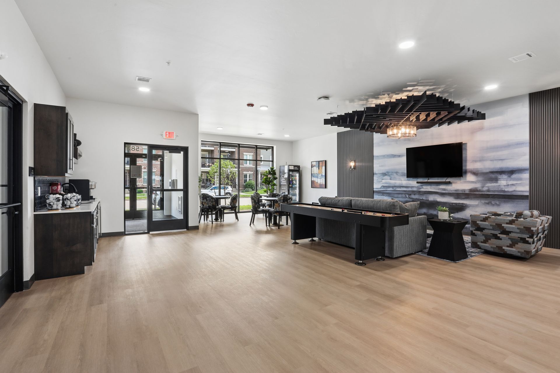 Modern open-plan living room with black sofas, TV, dining area, and large windows
