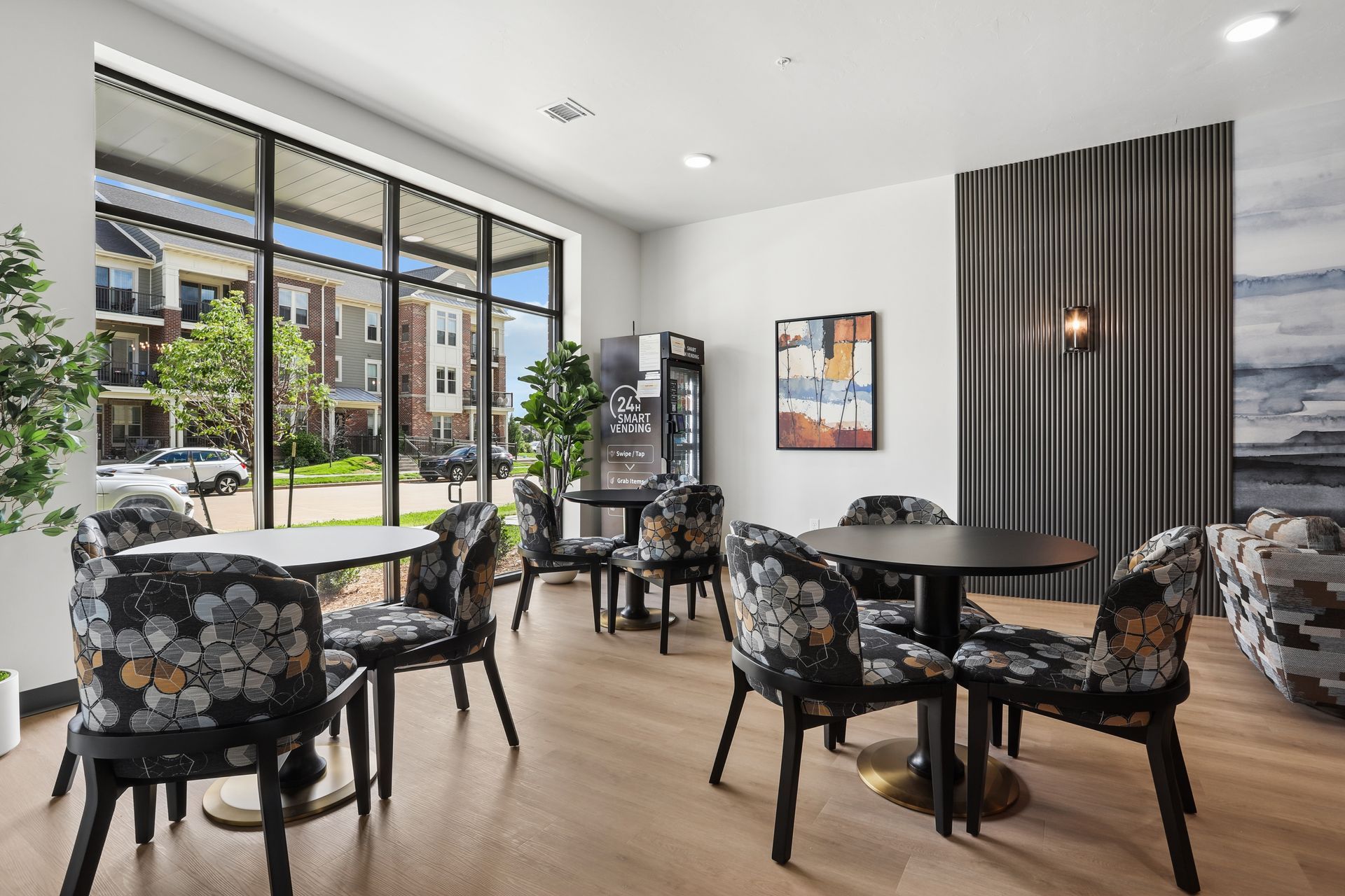 Modern cafe seating area with black chairs, round tables, and large windows overlooking greenery