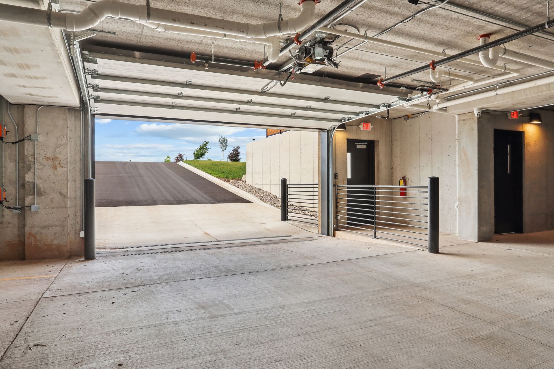 Underground parking garage with concrete floor, open exit ramp, and metal gate in a modern building