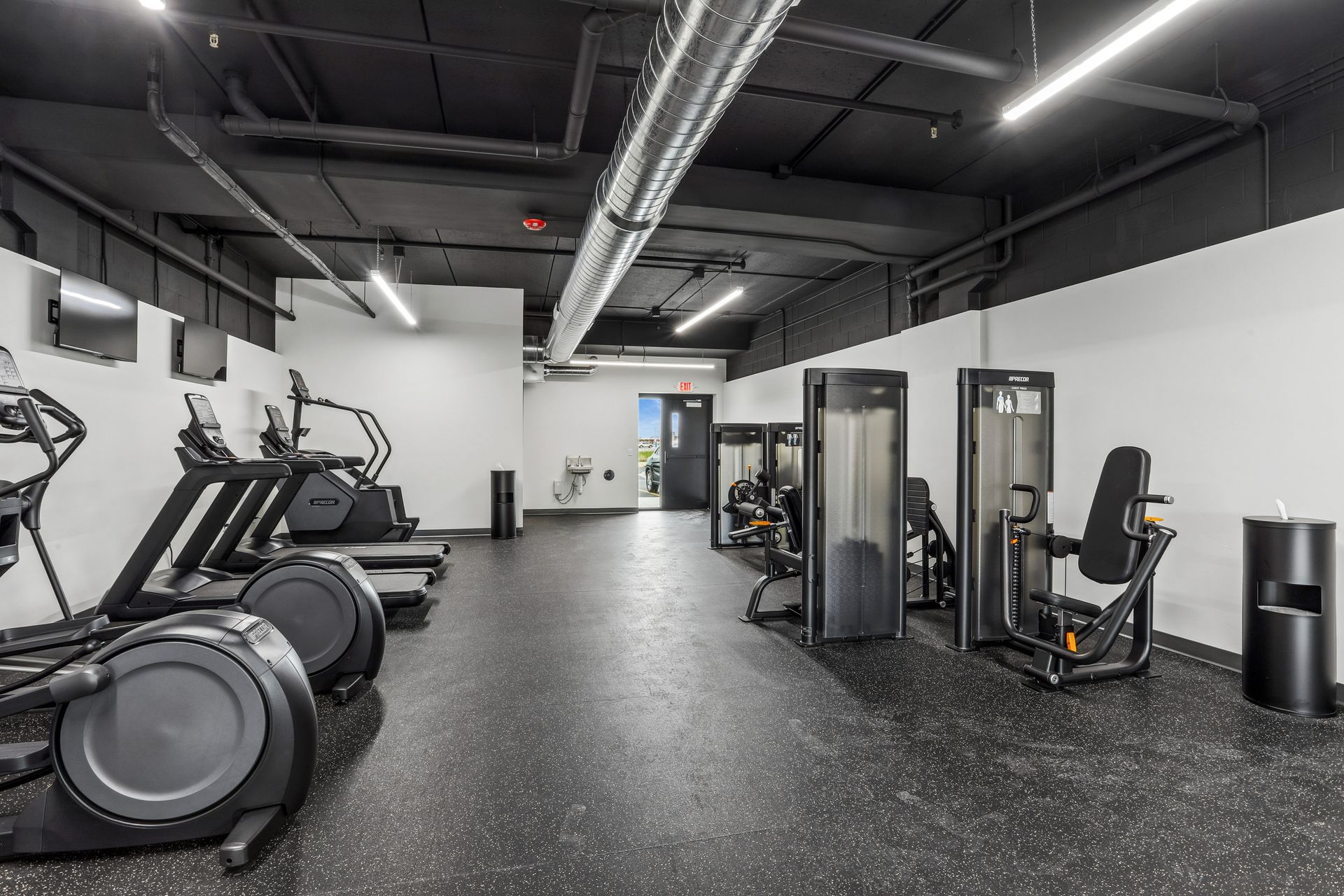 Empty modern gym with ellipticals, cable machines, and treadmills on a black floor.