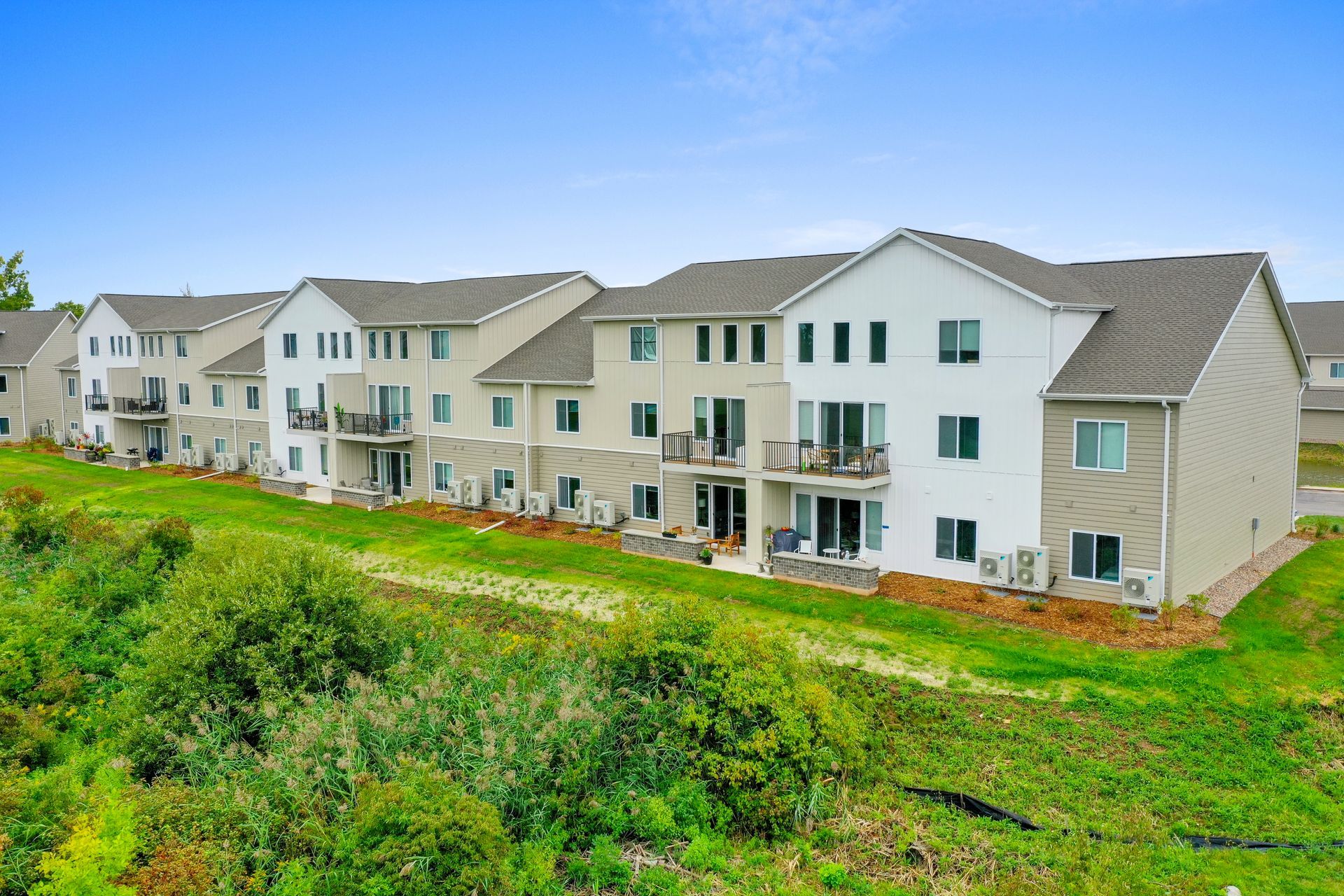 Row of beige apartment buildings beside a green grassy slope under a cloudy sky
