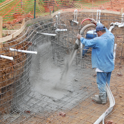 Construction worker spraying concrete into a curved pool frame.