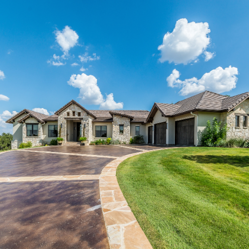 House with brown driveway, green lawn, and blue sky with clouds.