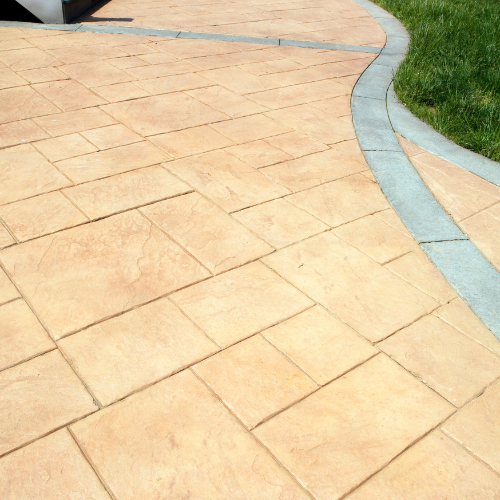 Tan stamped concrete patio with a gray border and grassy edge.