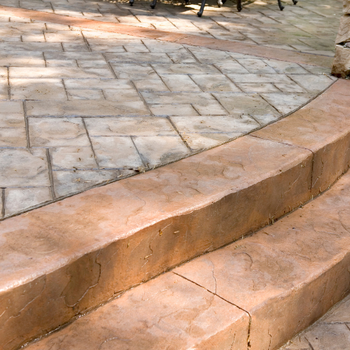Concrete patio steps with a decorative brick pattern and reddish-brown color.