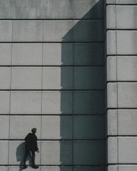 Person walking next to a textured concrete wall, with a long shadow cast by the sunlight.