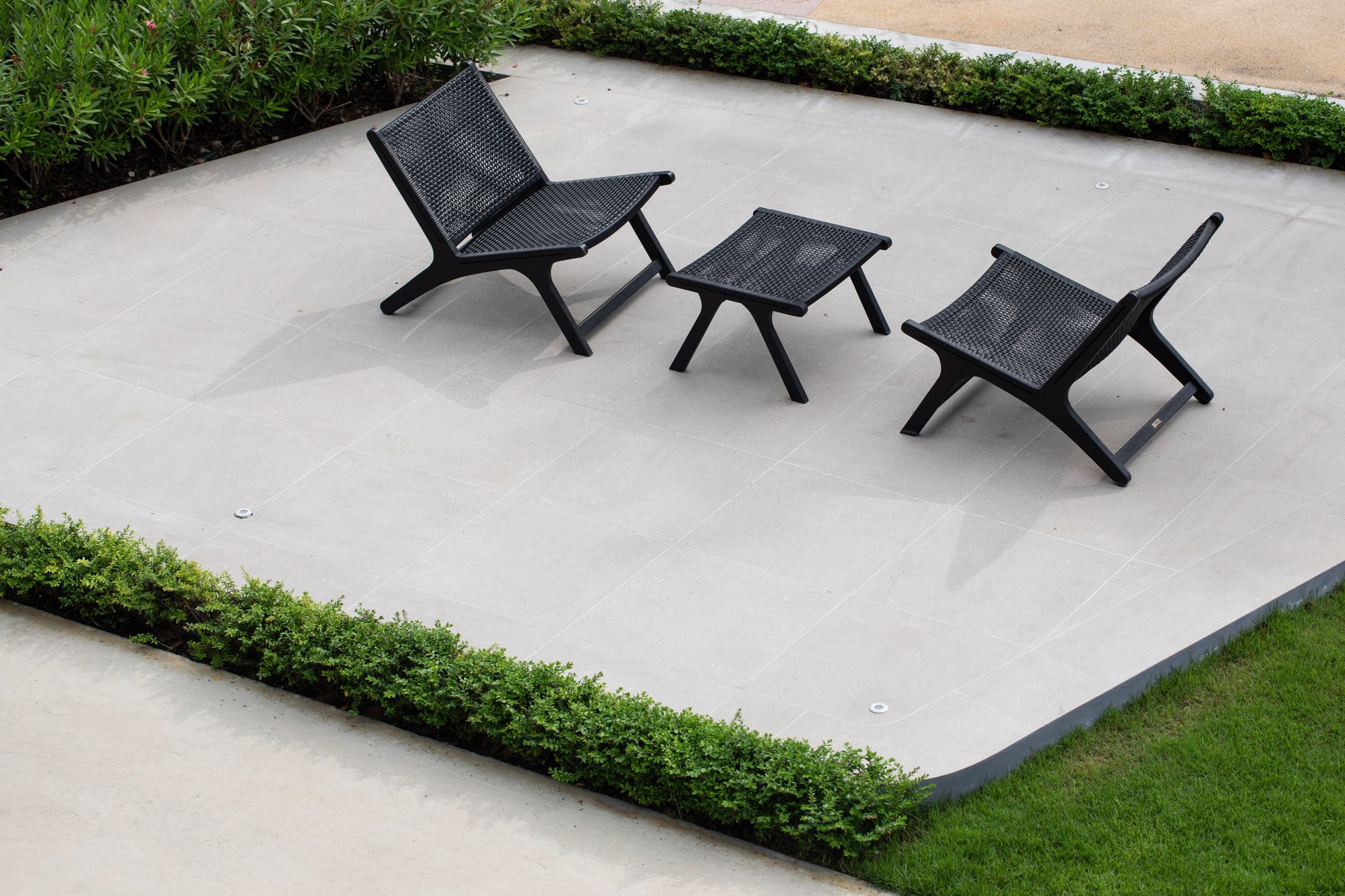 Patio with black outdoor furniture, surrounded by green grass and hedges.