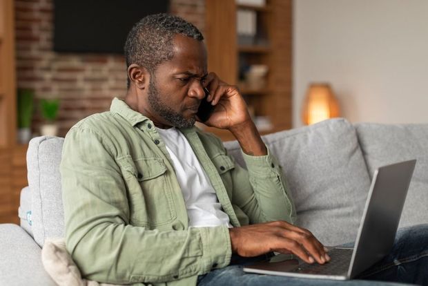 Person working on a laptop while talking on a smartphone in a living room