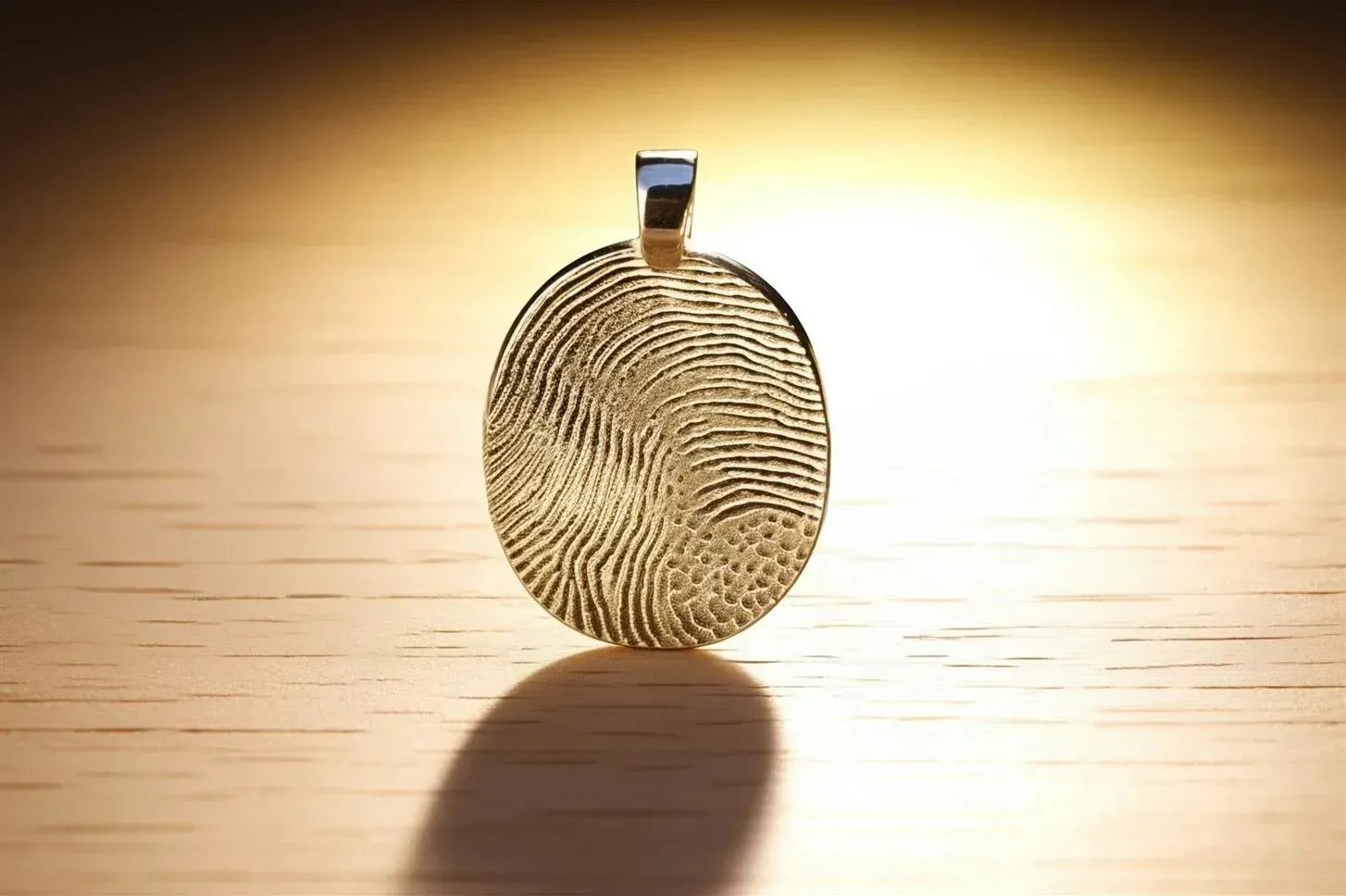 Oval pendant on a chain against a bright wooden surface, casting a long shadow