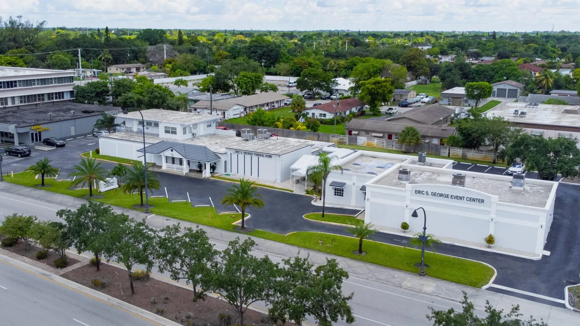 Aerial view of white apartment buildings along a tree-lined street in a suburban neighborhood.