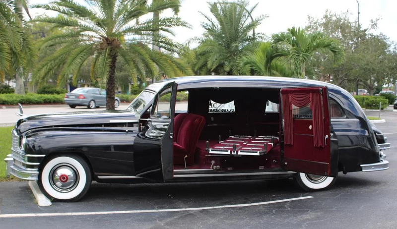 Vintage black hearse with maroon interior parked outdoors by palm trees