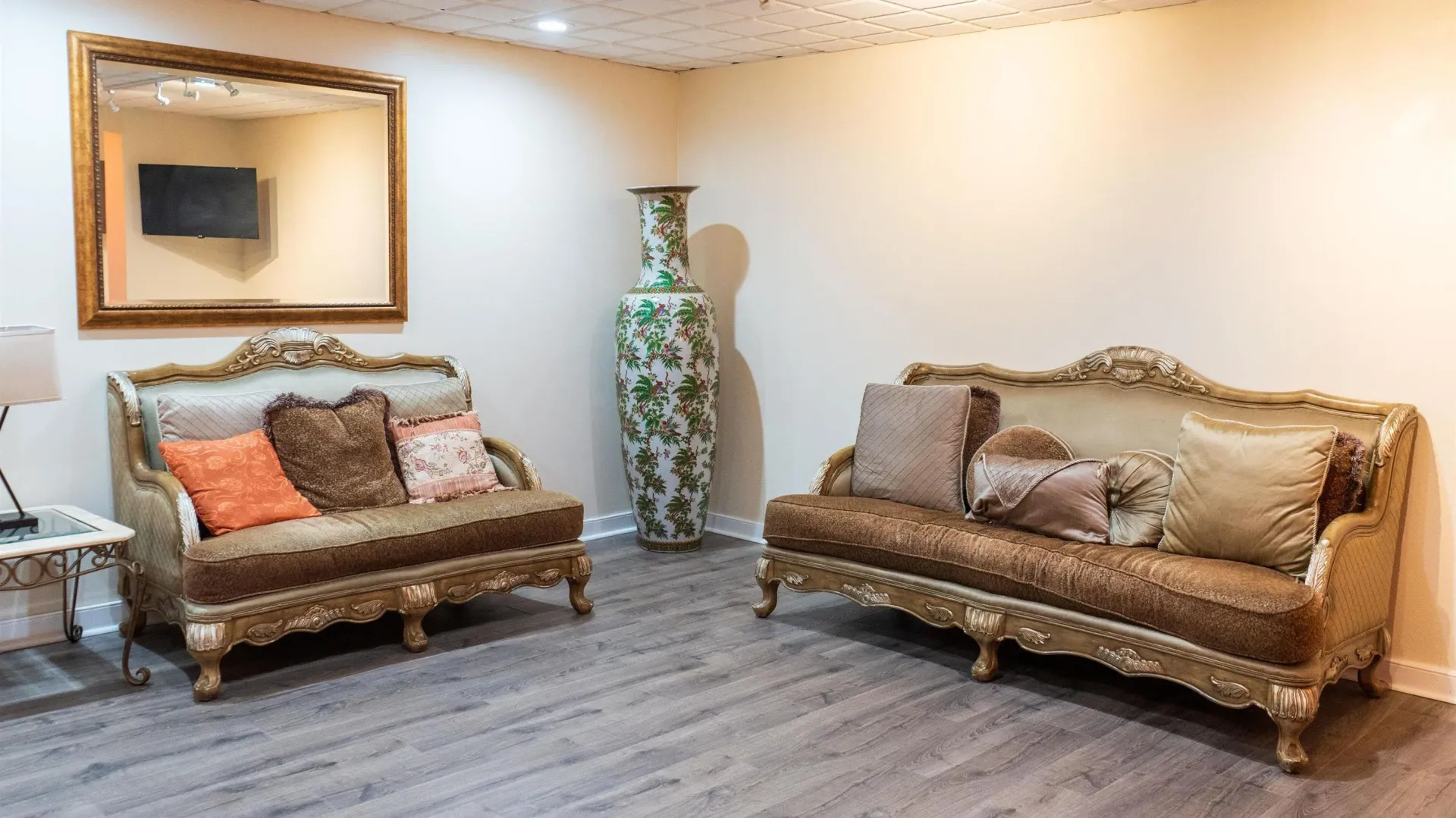 Elegant living room with two brown sofas, a large mirror, and a tall decorative vase