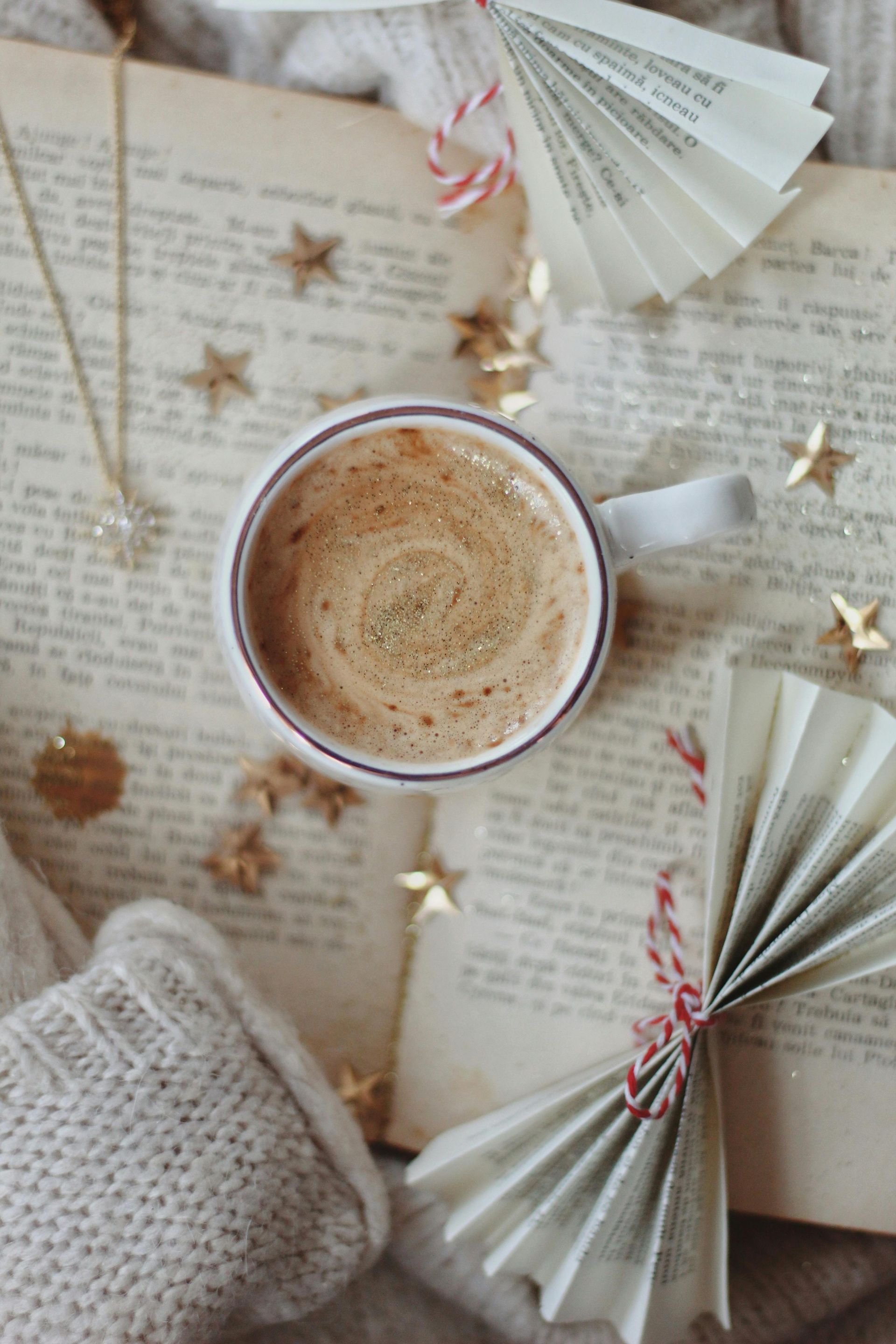 Cozy flat lay with a cup of coffee, folded book pages, and star decorations on an open book