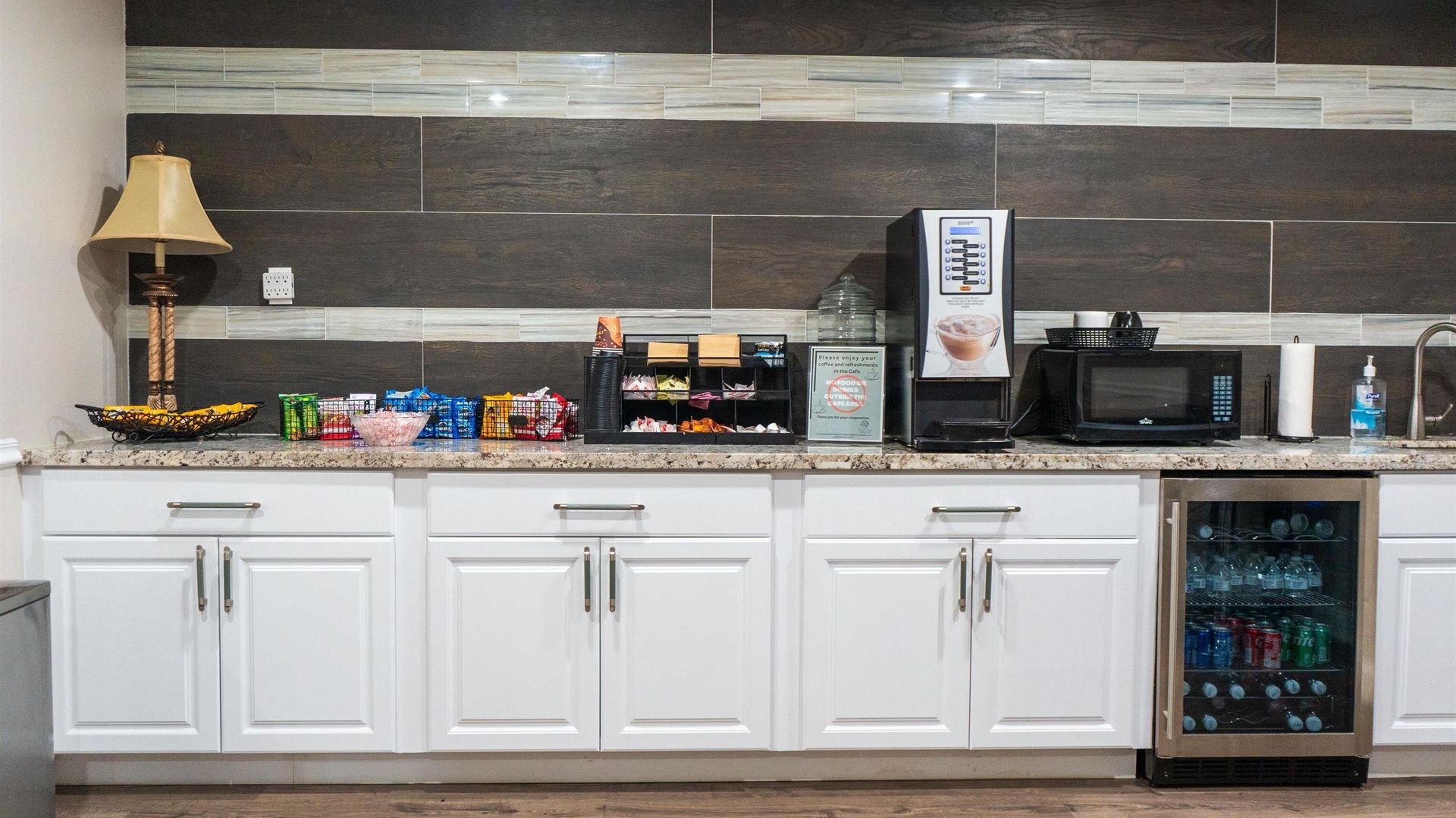 Break room counter with coffee maker, microwave, snacks, lamp, and mini fridge stocked with drinks