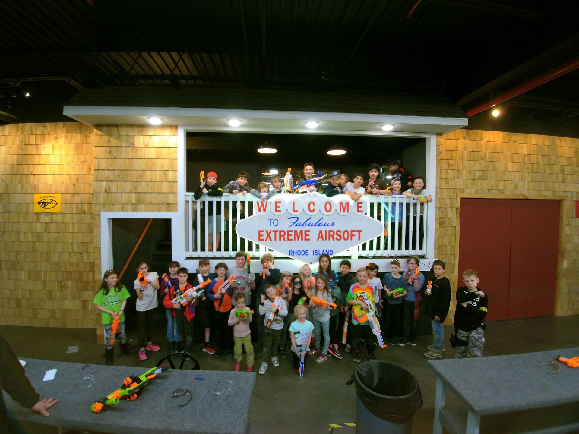 Group of children holding toy guns posing by a sign that says 