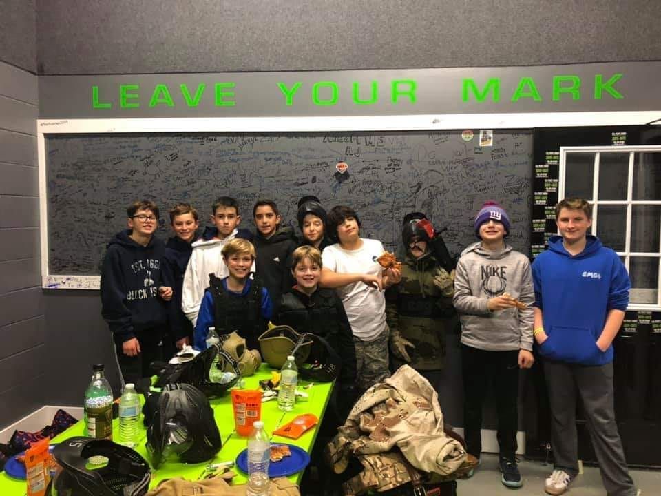 Group of young people in paintball gear pose under a 