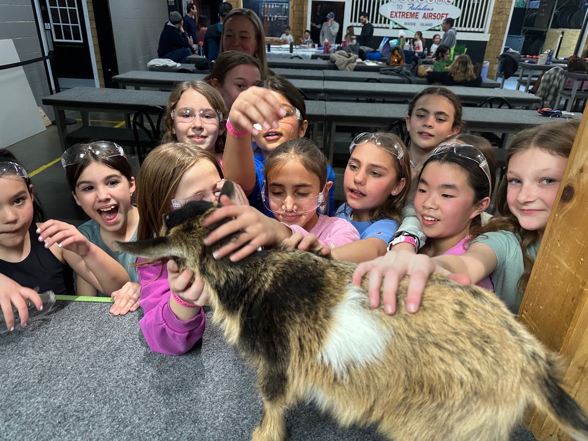 Group of children petting a goat; indoors, they're smiling and excited with white confetti in their hair.