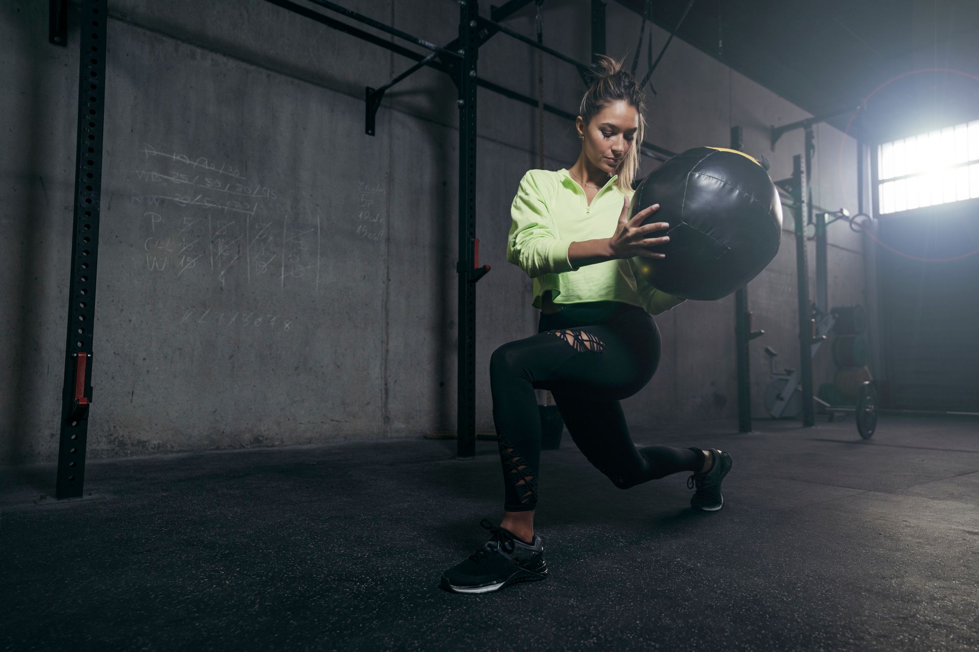 A woman is doing lunges with a medicine ball in a gym.
