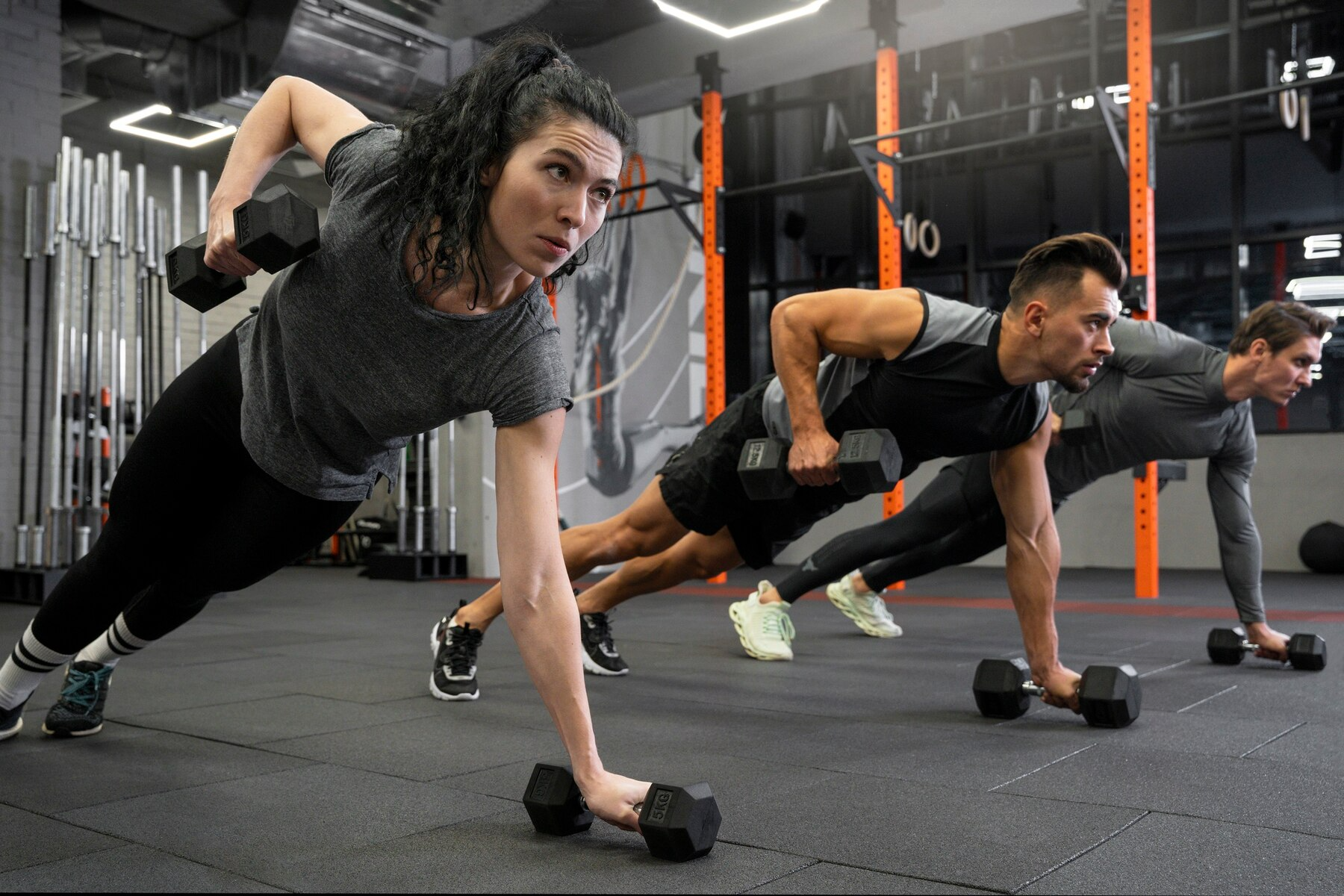 A group of people are doing push ups with dumbbells in a gym.