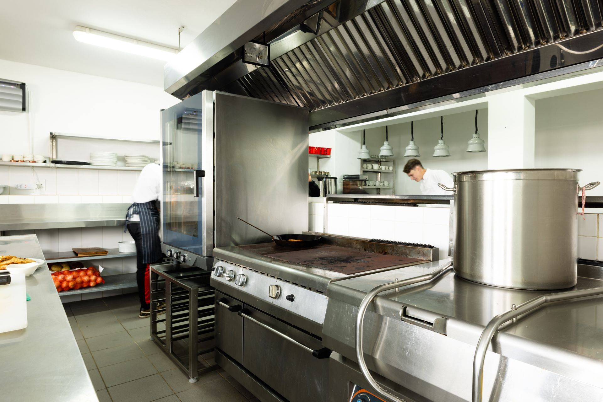 Commercial kitchen with steel cooking equipment, ventilation hood, and food preparation areas.