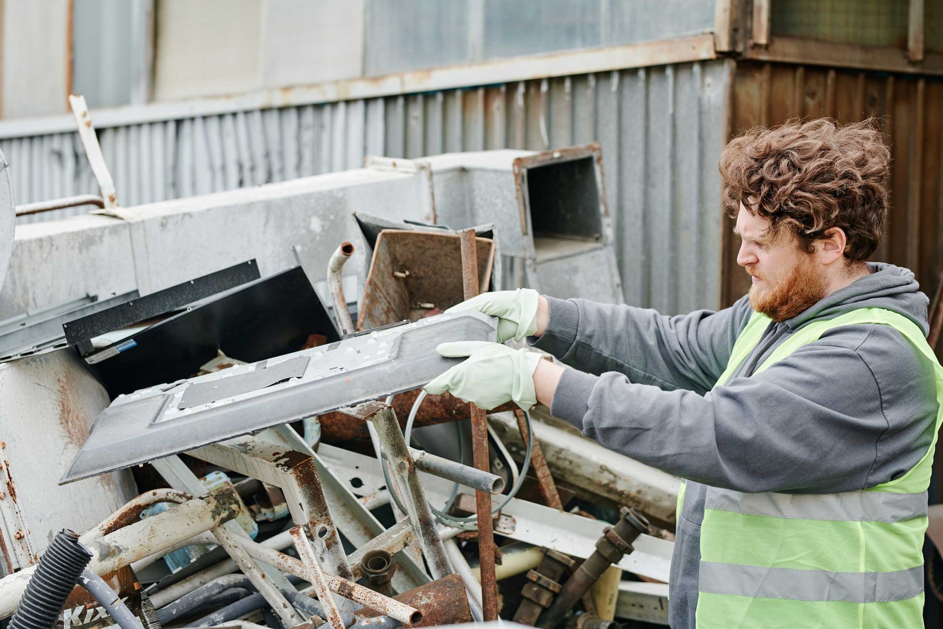 A worker is sorting collected scrap metals in a pile outdoors. A worker is sorting collected scrap metals in a pile outdoors.
