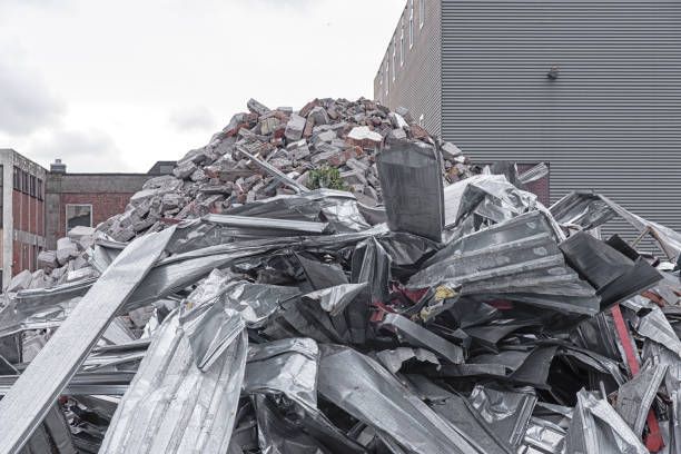 Pile of twisted scrap metal and rubble at a demolition site with buildings in the background.