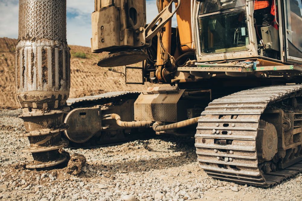 Construction vehicle with treads, drilling into a dirt mound. — Hannant Plant Hire in Ipswich, QLD