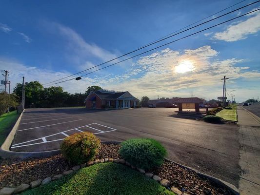 A sunny, wide-angle view of a paved parking lot in front of a brick building and a tall sign under a bright blue sky.