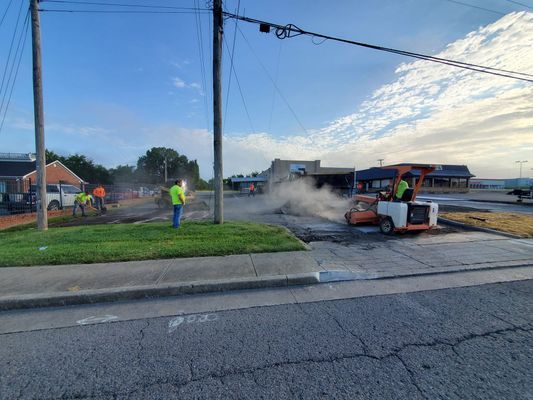 Construction crew using a road roller to pave an asphalt parking lot under a sunny sky.