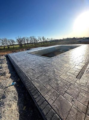 Stamped concrete pool deck with a gray slate pattern surrounding an empty rectangular swimming pool under a sunny sky.