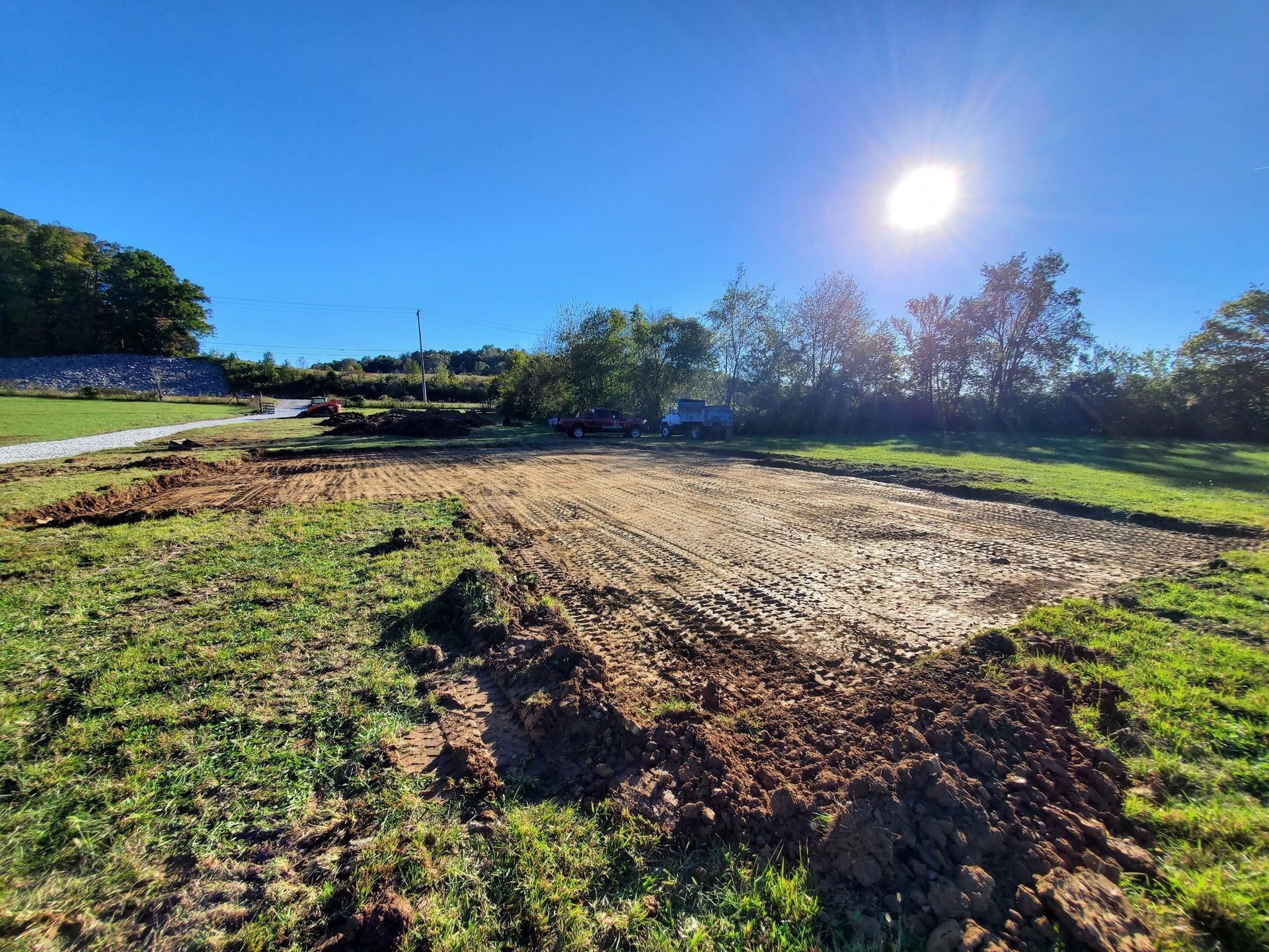 A leveled, dirt-filled rectangular construction site in a grassy field under a bright sun.