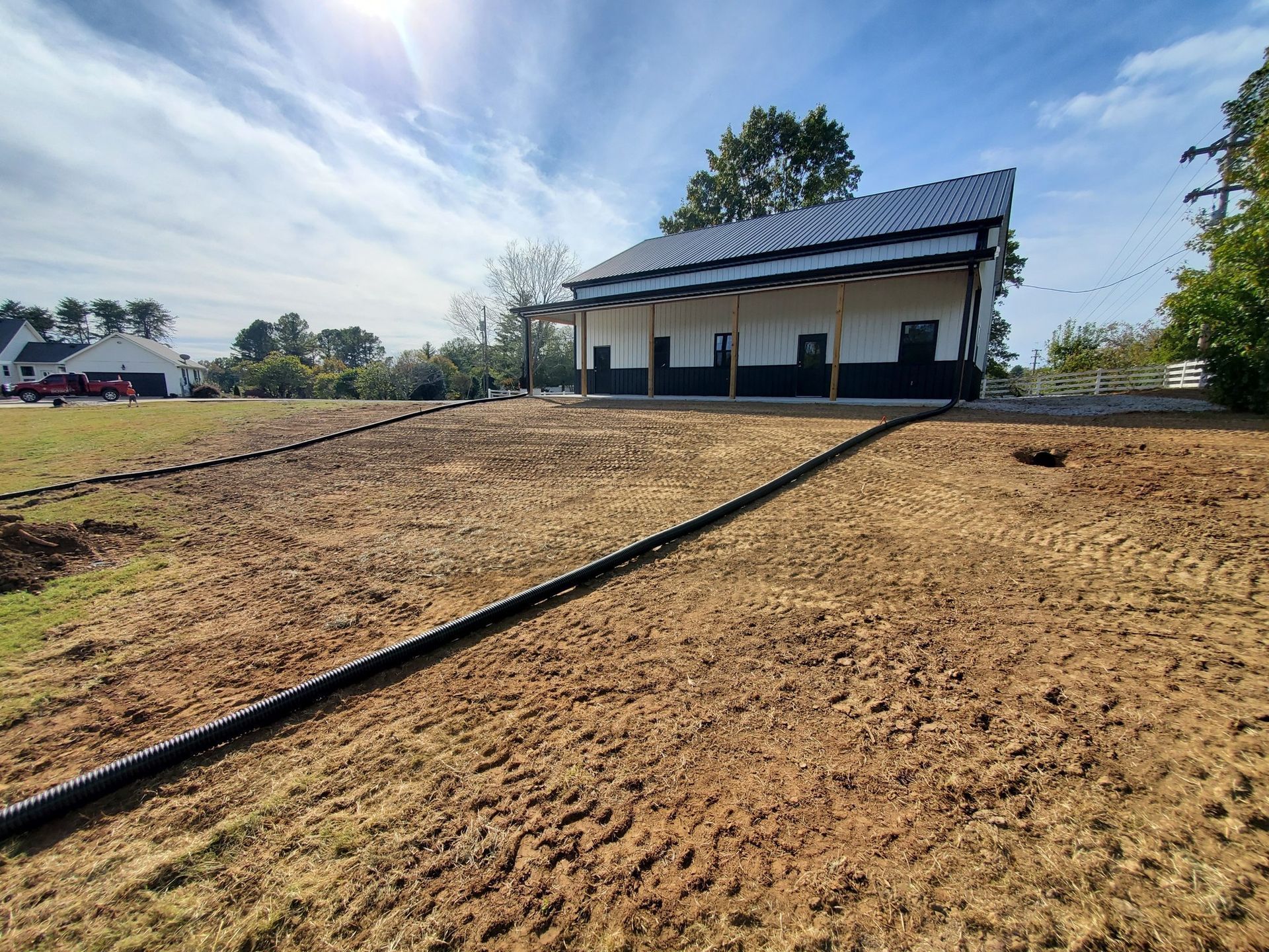 A white house with a dark roof and porch, situated on a large, freshly graded dirt lot with a black drain pipe extending out.