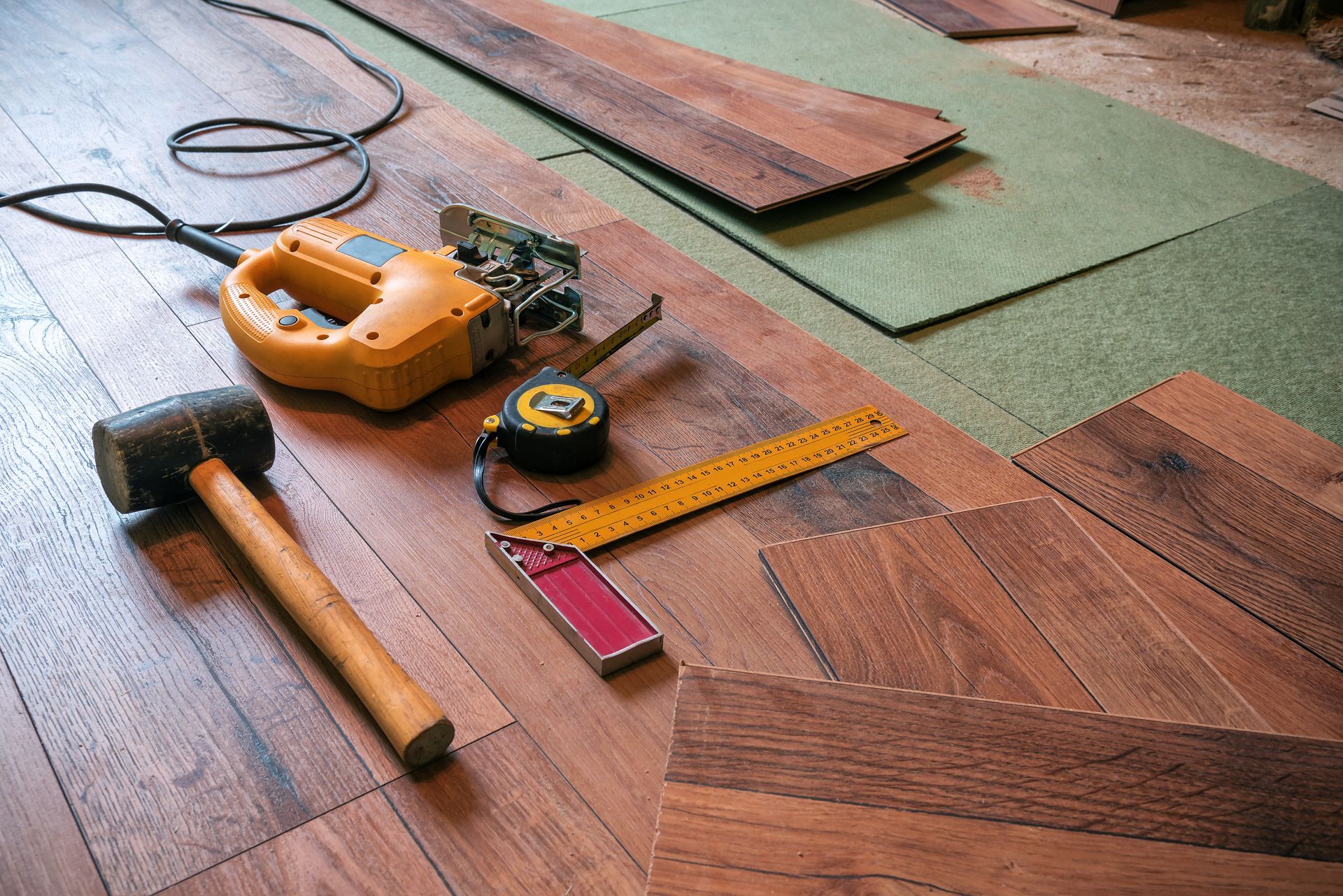 Tools and hardwood flooring in progress, including a mallet, saw, and tape measure.