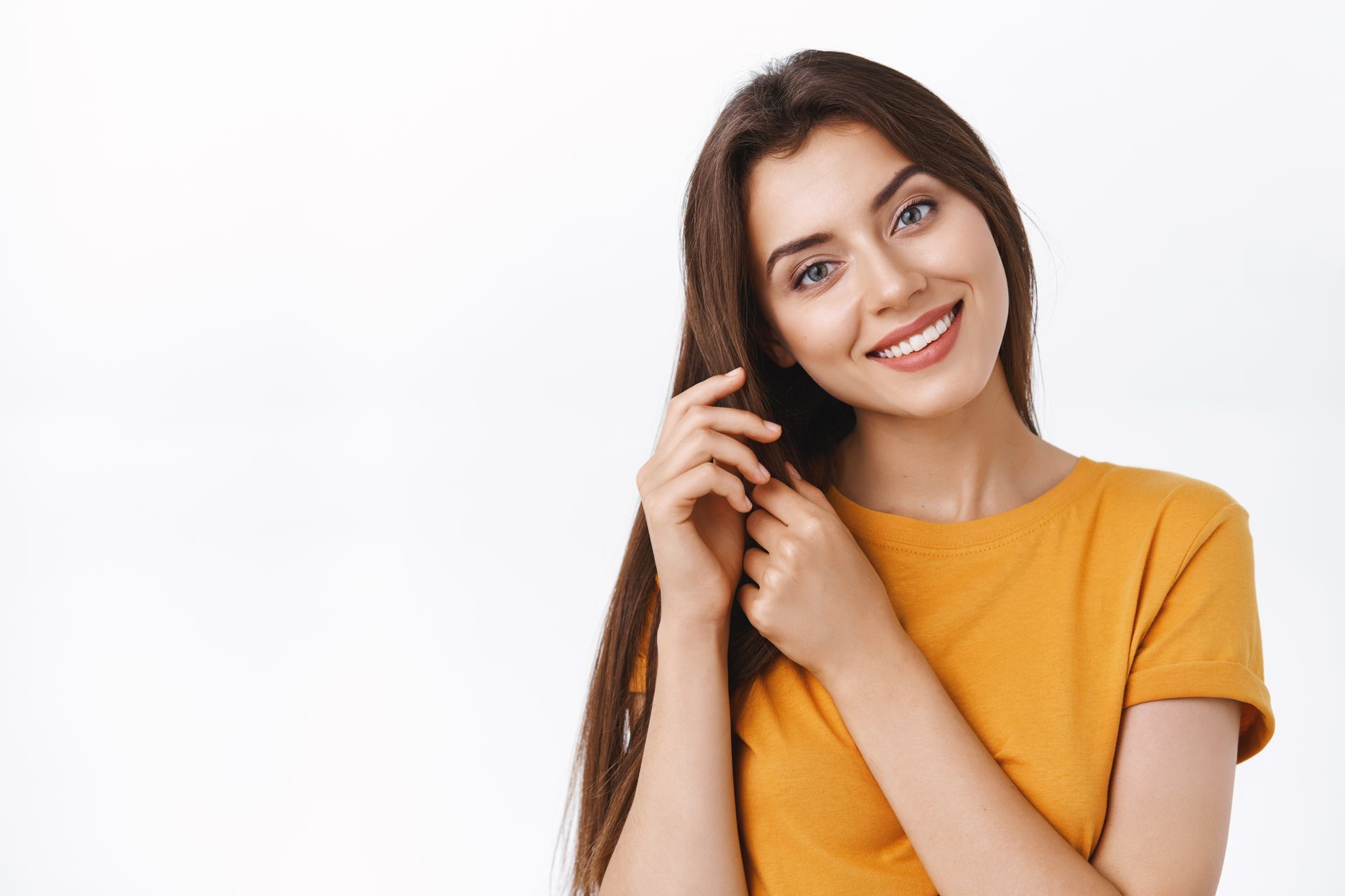 A smiling person with long dark hair wears a mustard yellow t-shirt against a plain white background.