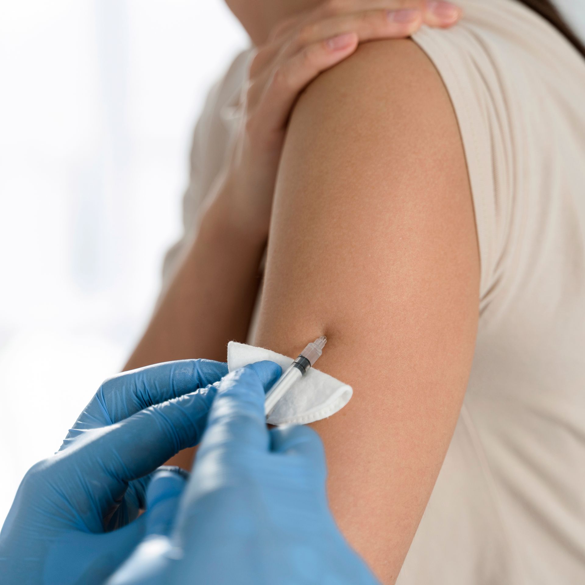 A person in blue medical gloves administers an injection into a patient’s upper arm.