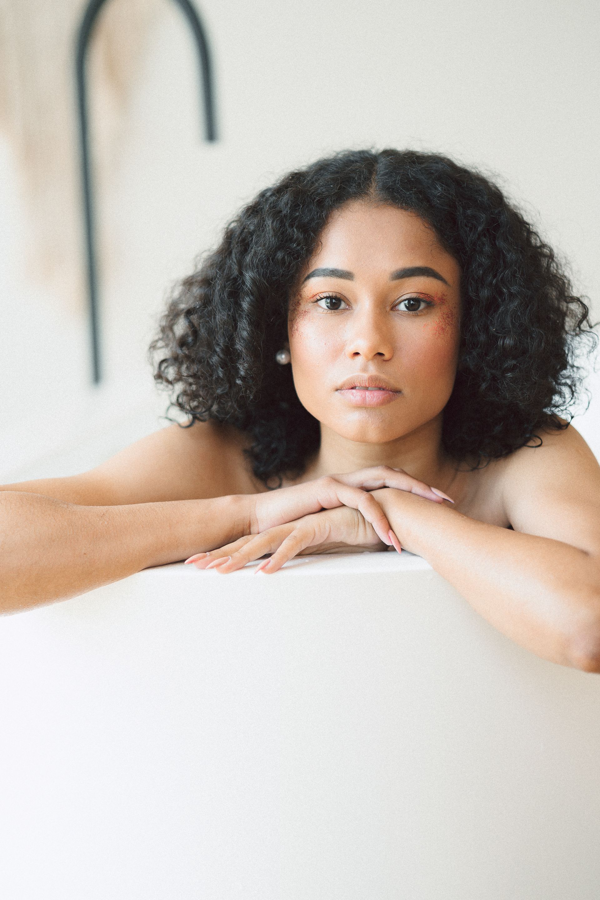 A person with dark, curly hair rests their chin on their hands while leaning over a smooth, white curved surface.