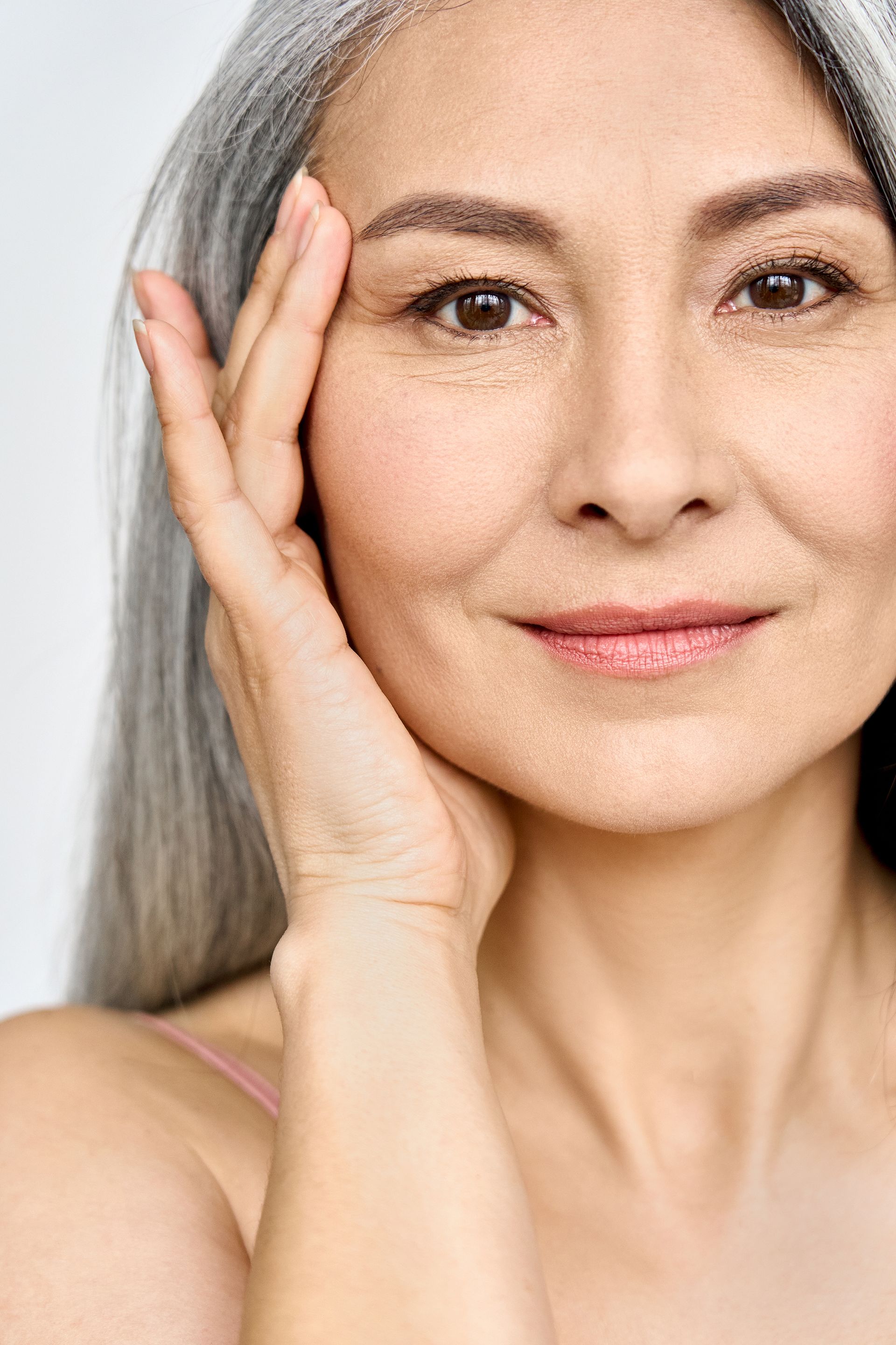 A person with grey hair gently touching their face with a hand, looking toward the camera with a calm expression.