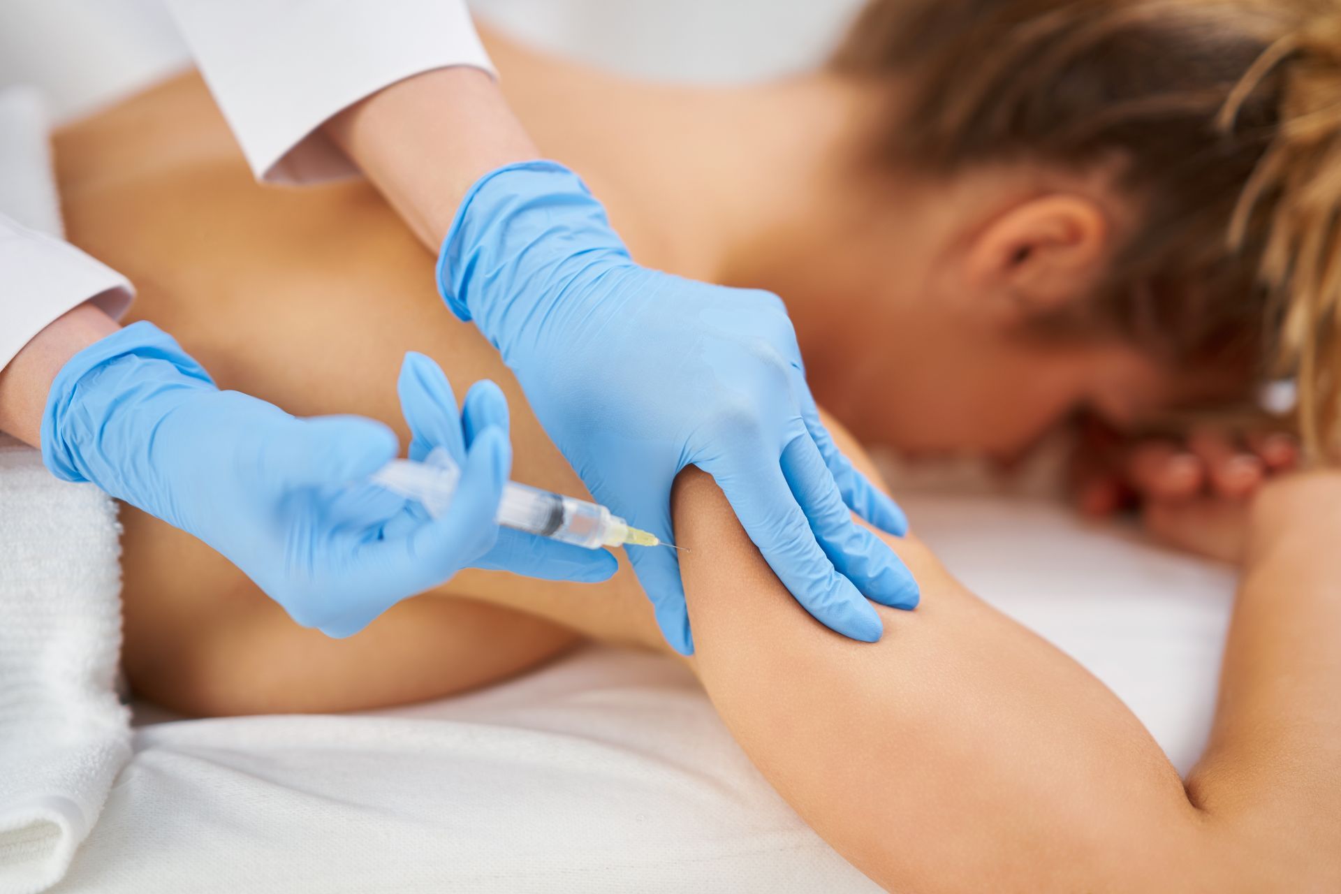 A medical professional in blue gloves administering an injection into a patient’s upper arm.