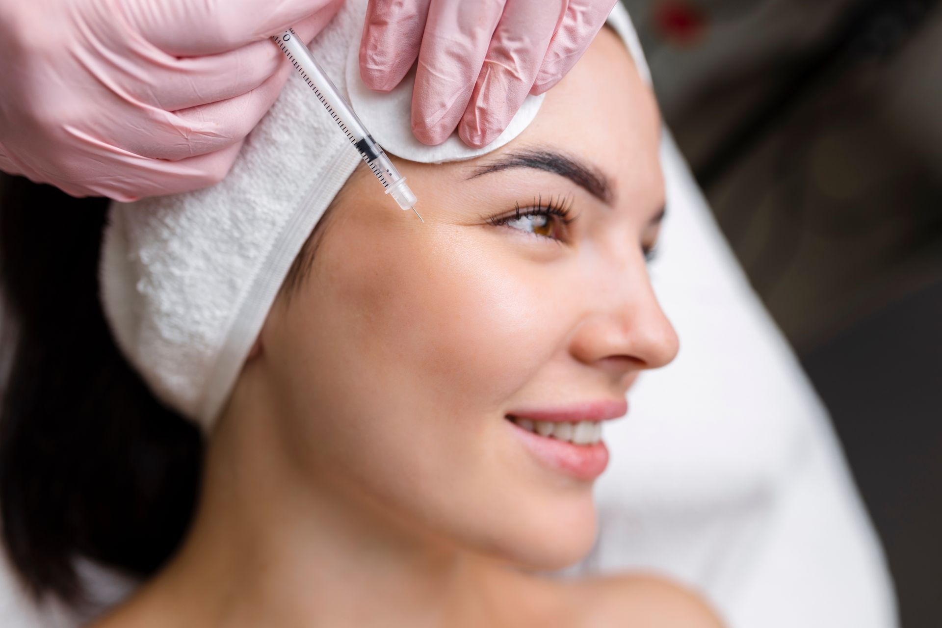 A person receiving a cosmetic injection near their eye from a professional wearing pink gloves.