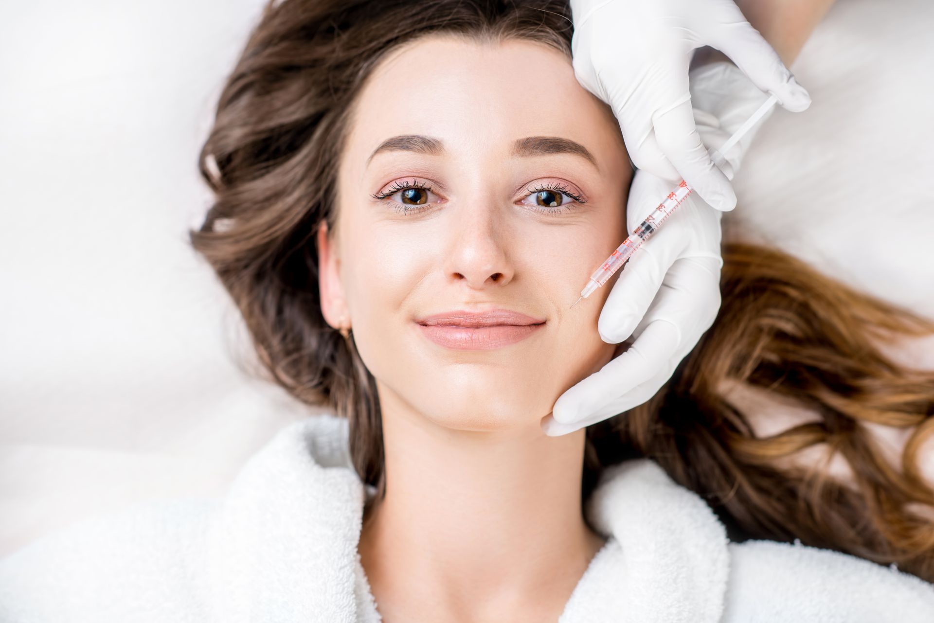 A person receiving a cosmetic facial injection from a professional wearing white medical gloves.