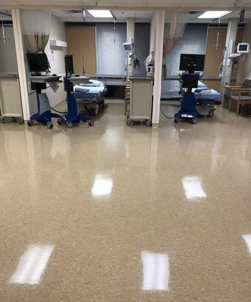 Hospital room with two beds, medical equipment, and shiny beige floor.