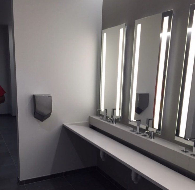 Modern restroom with wall-mounted hand dryers, sinks, long mirrors with lights, and a white counter.