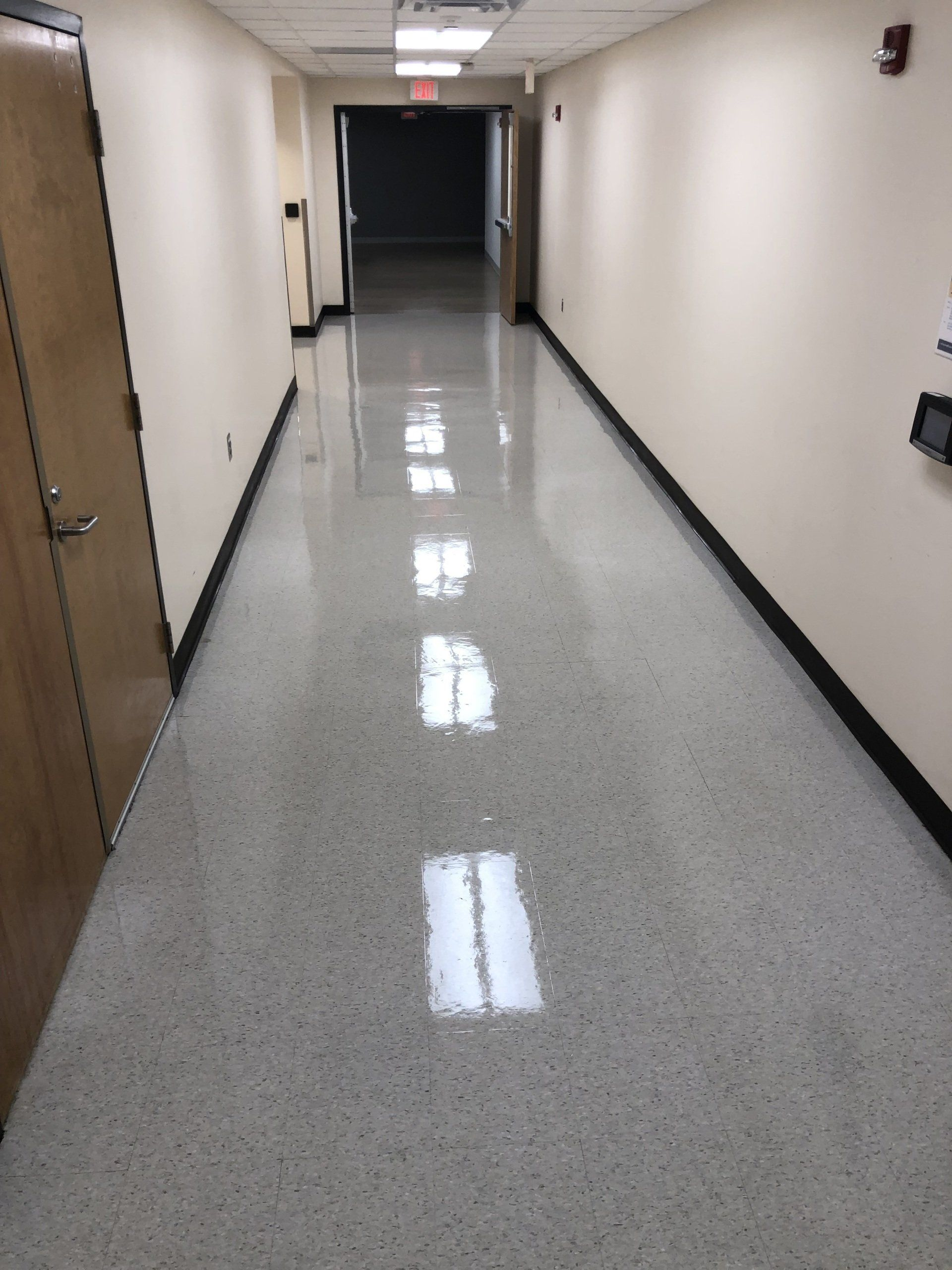 Long, empty hallway with shiny speckled floor, cream walls, and dark baseboards.