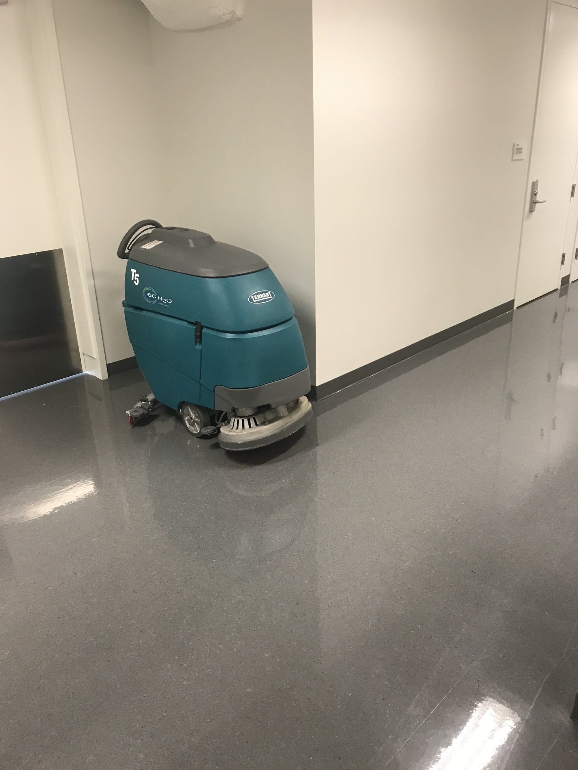 Teal floor cleaning machine in a hallway with shiny, gray floor.