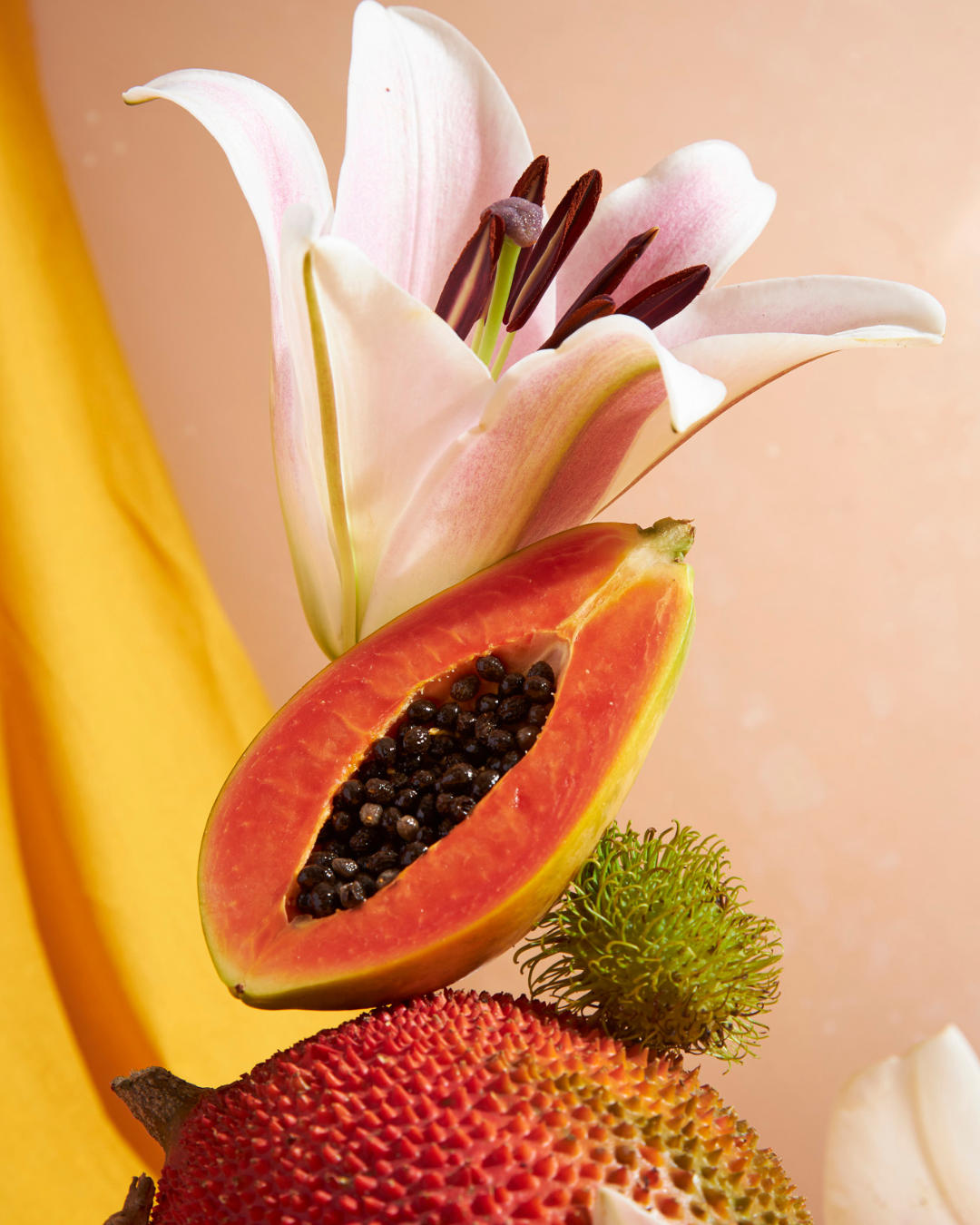 Rodaja de papaya, fresa y lirio blanco sobre un fondo suave color melocotón.