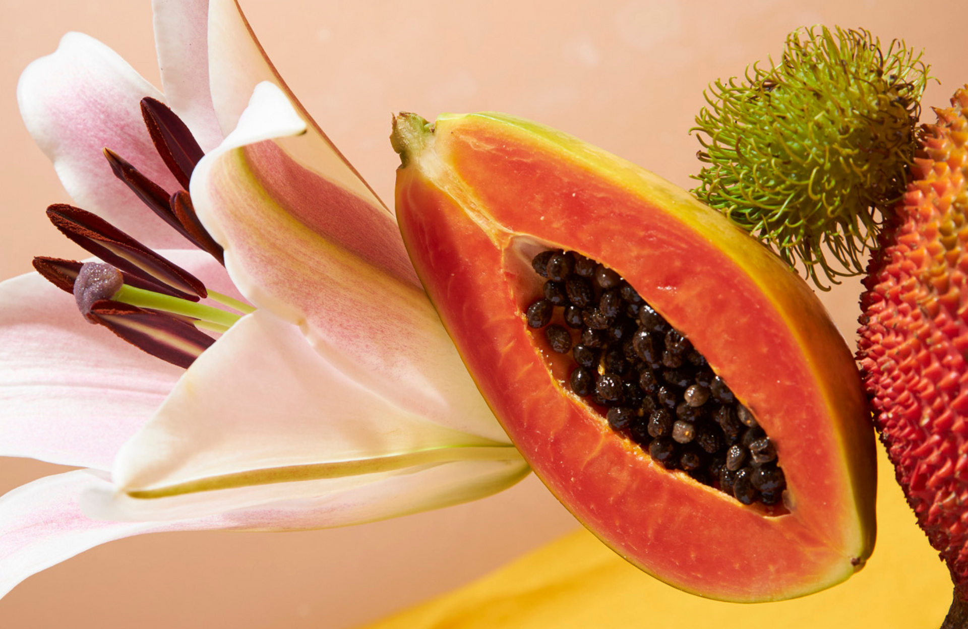 Frutas y flores tropicales dispuestas sobre un fondo amarillo brillante, con una papaya en rodajas y una fruta roja espinosa.