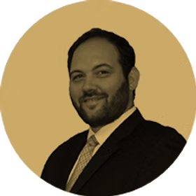 Man in suit smiling, with beard, in sepia-toned circle.