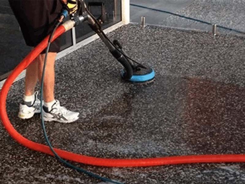 A Man is Cleaning a Concrete Floor With a Vacuum Cleaner — The Tile & Stone Specialists in Peregian Beach, QLD